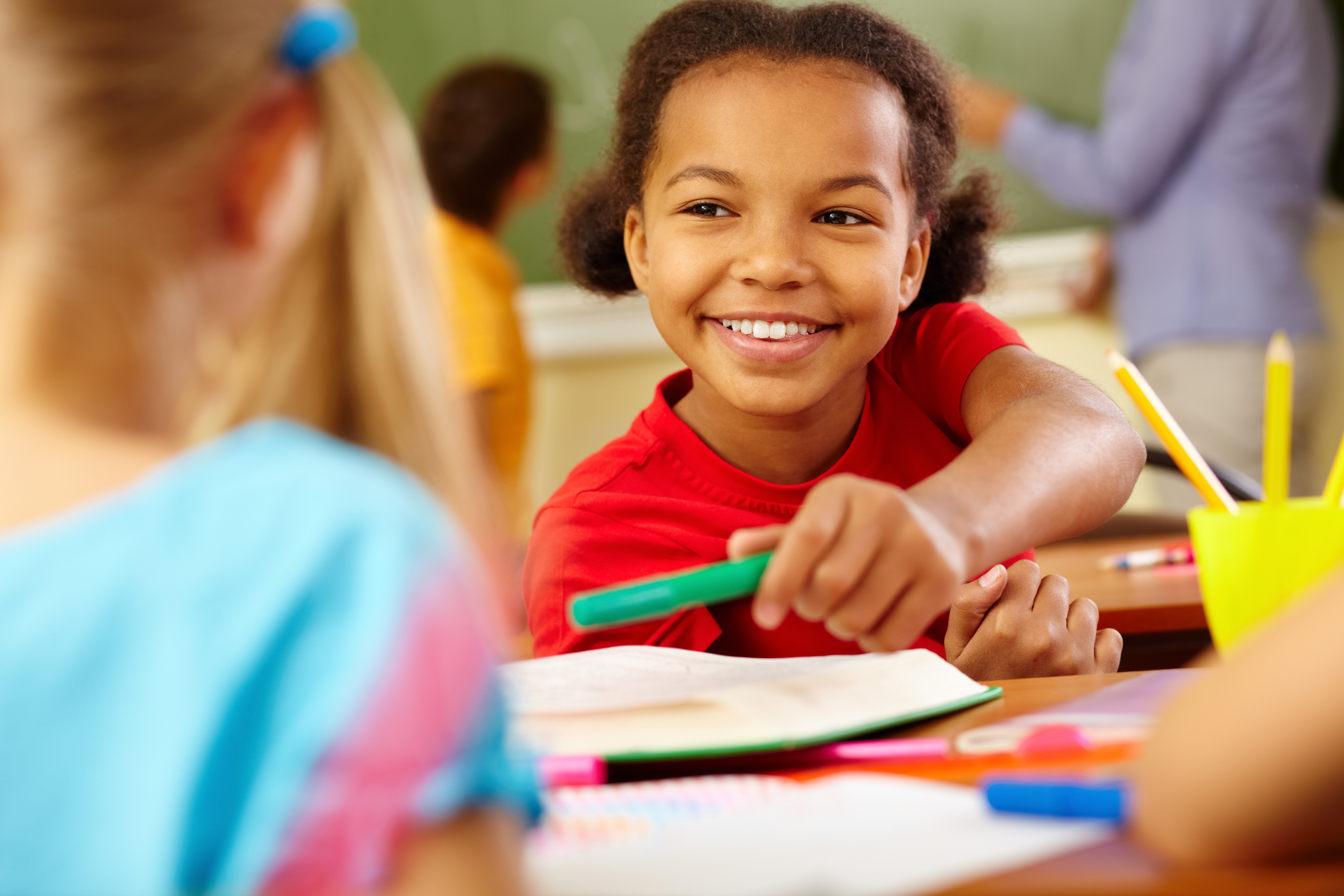 Portrait of cute girl giving crayon to classmate at lesson